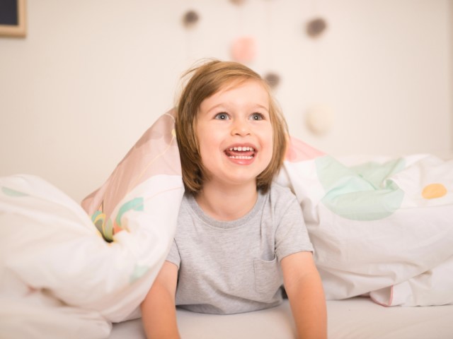 Happy boy with a big smile hiding under bedding set with Jeanette the Cat